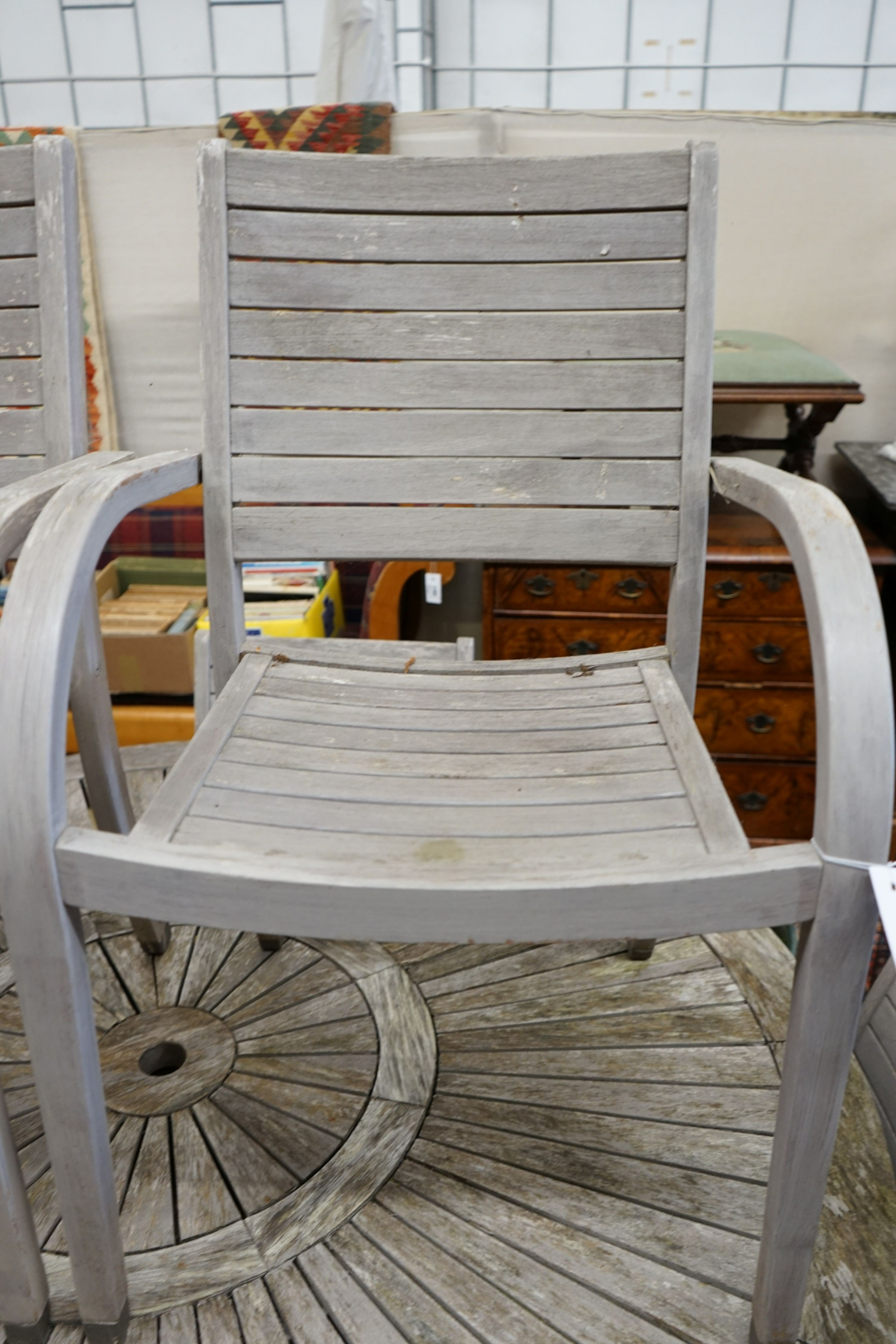 A circular weathered teak garden table, diameter 153cm, height 75cm together with six weathered teak stacking garden elbow chairs